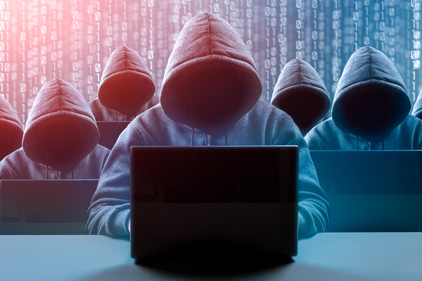 Group of hooded figures bent over a laptop trying to access the dark web