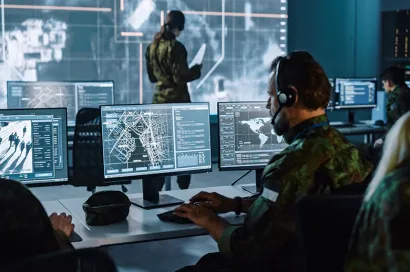 Two individuals in a high-tech control room monitoring global data, with one person facing large screens displaying maps and another person seated at a desk with multiple monitors.